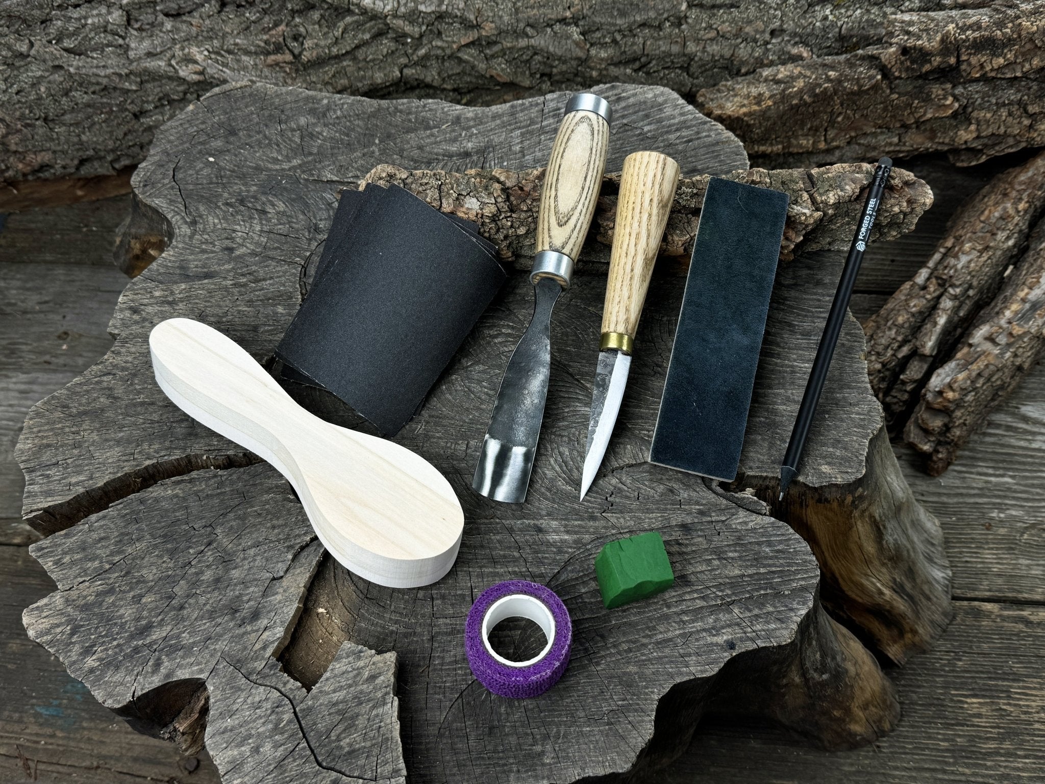 Spoon carving kit with sharpened tools, wooden blank, sandpaper, sharpening board, pencil, and finger wrap
