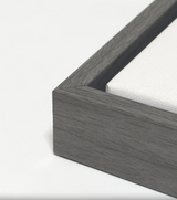 Close-up of a dark gray wooden frame corner holding a white textured canvas, showing clean mitered edges and smooth wood grain.