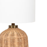 Table lamp with a rounded woven rattan base in natural beige tones and a large white fabric drum shade, accented by a brass connector at the top of the base.