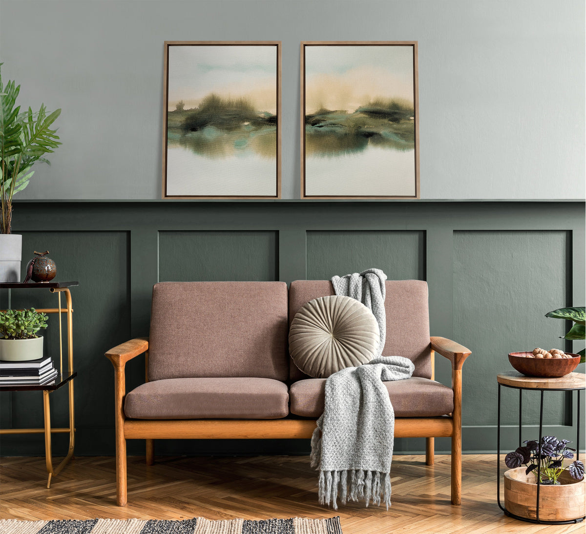 Living room with wooden-framed mauve loveseat, round beige pillow, gray knit throw, abstract green-beige framed art, olive green wainscoting, and plants on side tables.