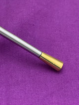 Close-up of a silver metal rod with a polished gold-colored tapered tip, resting on a textured purple fabric background.