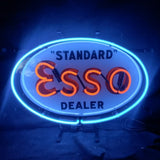 Oval neon sign with bright blue border, glowing orange letters spelling 'Esso,' and black text reading 'STANDARD' above and 'DEALER' below the logo on white background.