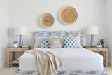 Bedroom with white bed featuring a weathered blue-gray headboard, blue starburst-patterned pillows, beige woven round wall baskets, and matching side tables with blue lamps.