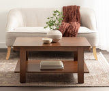 Rectangular wooden coffee table with a lower shelf holding stacked books, placed in front of a light beige sofa with wooden legs and a textured rust-colored throw blanket.