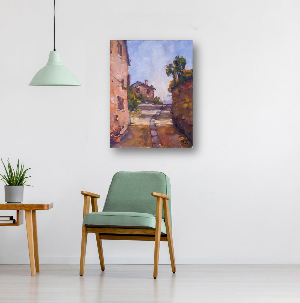 Impressionist canvas painting of a sunlit pathway between stone buildings, framed by greenery and a pale blue sky, hanging above a light green armchair.