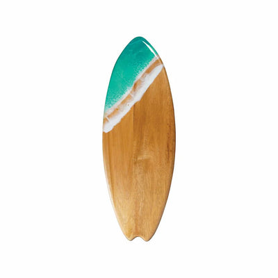 Wooden surfboard-shaped charcuterie board with blue resin accent, holding cheese and fruit on a patio table