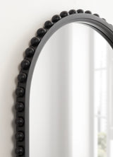Arched wall mirror with a matte black frame adorned by a row of evenly spaced spherical beads along the top curve, reflecting a bright window.
