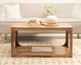 Rectangular wooden coffee table with smooth top and curved side cutouts, decorated with a white vase holding greenery and stacked neutral books, set on a patterned rug in front of a beige sofa.
