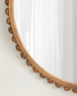 Close-up of a round wooden wall mirror with evenly spaced spherical wooden beads around its frame, reflecting a white curtain.