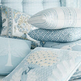 Stack of decorative pillows in spa blue tones featuring varied patterns including florals, geometric designs, and a dragonfly motif with soft fabric textures.