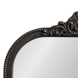 Top corner of an arched mirror featuring a dark ornate frame with beaded trim and intricate carved scroll detail at the crest.