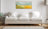 Framed rectangular canvas above white sofa, depicting abstract landscape with sky-blue, golden yellow, and green shades on a minimalist off-white wall.