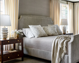Gray-upholstered bed with curved headboard, dressed in gray bedding and leopard-patterned pillow covers, flanked by dark wood nightstands with ceramic lamps.