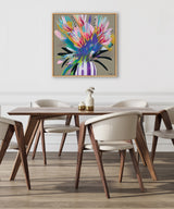 Square framed canvas with an abstract bouquet of pink, blue, green, and yellow flowers in a striped purple and white vase, hanging above a modern dining table with four white chairs.