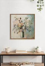 Framed canvas painting of a botanical arrangement with pastel-colored flowers and green leaves in a glass vase, hanging above a wooden table with neutral decor.