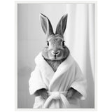 Black and white photo of a rabbit wearing a white bathrobe, standing upright against a simple backdrop with a soft curtain, showing its ears pointed up and hands tucked in the robe.