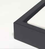 Close-up of a black wooden frame corner with white canvas stretched inside, showing the clean edge and fine texture of the canvas.