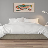 Framed horizontal canvas above bed features a stylized fish in orange, green, and peach tones with two fishing lures on beige linen-textured background.