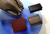 Drawstring pouch and three small wallets featuring geometric triangle patterns in black with red or beige, displayed on a round blue glass surface.
