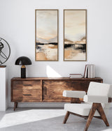 Two vertical abstract landscape paintings with soft beige, black, and white tones framed in wood above a wooden sideboard and modern white armchair in a bright room.