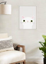 Minimalist framed illustration of a white cat with large green eyes and pink ears, hanging on a light beige wall above a cream armchair and green potted plant.