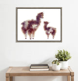 Framed canvas art showing two stylized alpacas with fluffy, cloudlike bodies in shades of brown and cream against a white background, hung above a wooden table with plants and books.