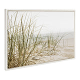 Framed canvas print showing sandy beach with tall, thin green grass in foreground and soft, muted ocean waves in the background under a pale sky.