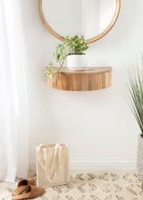 Round floating wall-mounted wood side table with vertical grain, holding a white pot with a trailing green plant, beneath a round wooden-framed mirror.