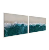 Two framed canvas prints depicting aerial views of ocean waves crashing onto a sandy beach, with deep teal water transitioning to white foam and beige sand, side by side.