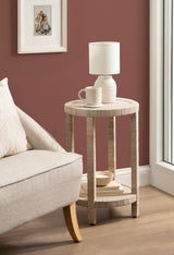 Round wooden side table with slatted design, holding a white textured lamp and ceramic mug, positioned beside a beige sofa against a muted red wall.
