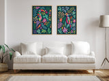 Two vibrant framed canvas prints featuring colorful tropical parrots and foliage in pink, yellow, green, and blue hues, hung above a white sofa in a minimalist living room.