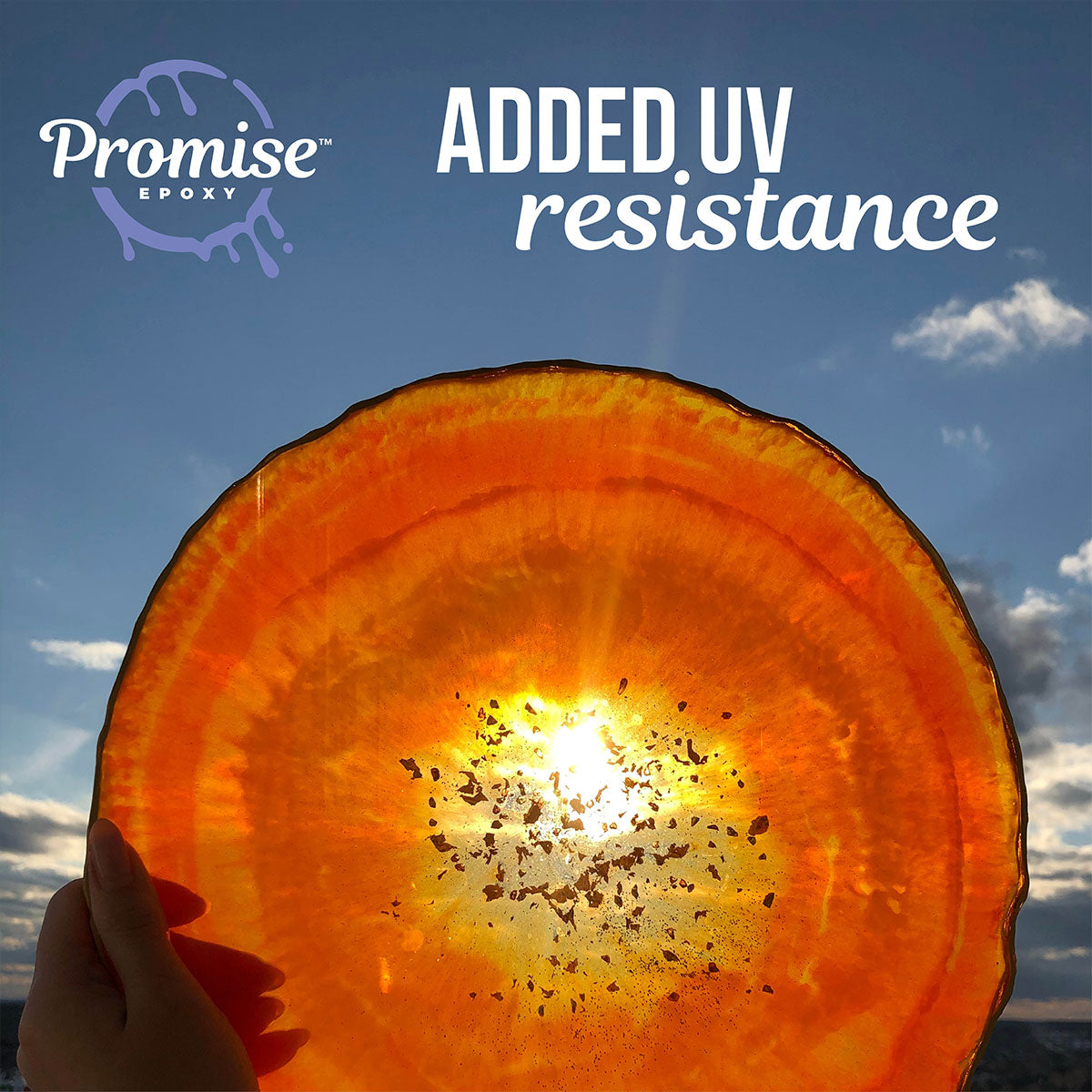 Hand holding a translucent orange resin disc with dark flecks, backlit by sunlight against a blue sky with clouds, highlighting UV resistance.