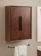Rectangular wall-mounted wooden bathroom cabinet with two doors and tall vertical handles in matching wood tone, set against a beige wall above a black towel bar with a white towel.