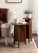 Two dark wood side tables with curved legs and clover-shaped tops, one holding a white potted plant and the other a cup and book, set beside a beige upholstered chair.