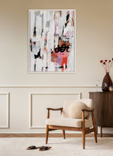 Abstract framed canvas with textured white, pink, rust, and black brush strokes above a mid-century modern armchair with cream upholstery and wooden arms, next to a dark wooden cabinet with a tall brown vase and dried flowers.