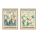 Two framed canvas prints by Carrie Cantwell featuring stylized flowers labeled 'Flower Market Amsterdam' with tulips on blue, and 'Flower Market Copenhagen' with daisies on light green backgrounds.
