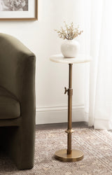 Round white marble top adjustable plant stand with brushed gold metal base and vertical support, holding a white ceramic vase with small dried branches next to a green sofa.