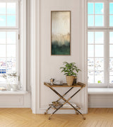 Tall vertical abstract canvas with gradient shades of cream, brown, and green hanging above gold and wood bar cart holding a potted plant, cups, and bowls in a bright room with tall windows.