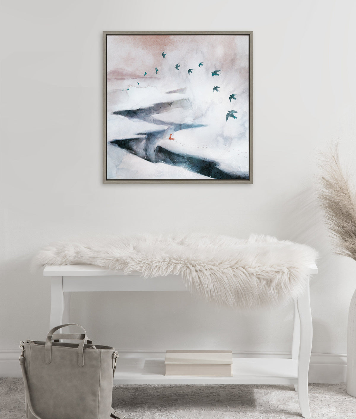 Framed canvas of a snowy landscape with a fox at a river bend and a flock of birds flying diagonally across a misty sky, hung above a white bench with a fluffy cover.