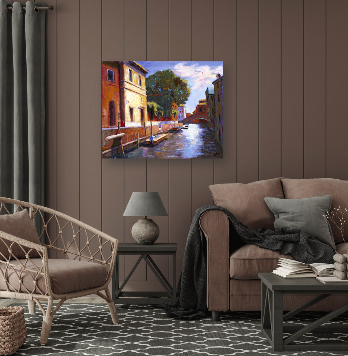 Colorful canvas print of a Venice canal with buildings, a tree, and a distant bridge, hung on a brown paneled wall above a gray lamp and brown sofa.