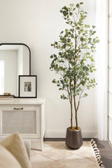 Tall faux eucalyptus tree with round green leaves in a dark round planter, placed next to a white cabinet with a cane front and a black-framed picture and mirror.
