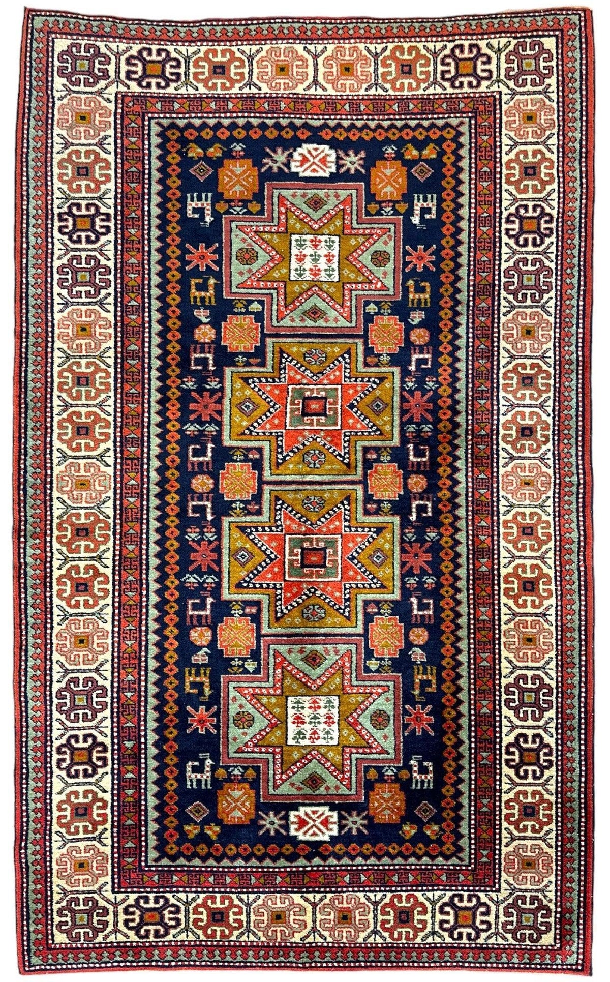 Vintage Armenian Karabakh rug with a deep blue center featuring four large star motifs in orange, green, and red, surrounded by intricate geometric borders in cream, red, and brown.