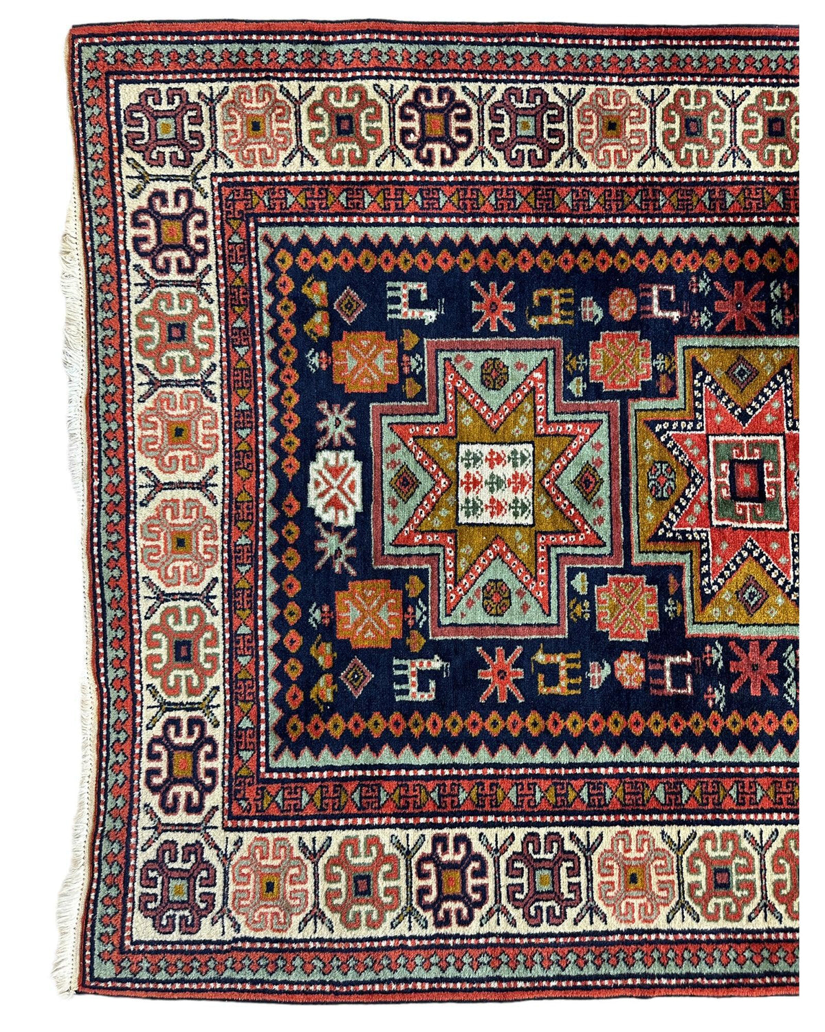 Corner of a vintage Armenian Karabakh wool rug featuring intricate geometric star motifs in green, orange, and red on a dark blue field, framed by a multi-patterned cream border.