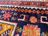 Close-up detail of a vintage Armenian Karabakh/Artsakh wool rug featuring dark blue background with geometric patterns in red, orange, white, and yellow.