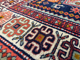Close-up of a vintage Armenian Karabakh wool rug showing geometric motifs in red, cream, blue, and orange with a rich, textured pile.