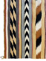 Section of a vintage Navajo rug with vertical stripes featuring chevron and zigzag patterns in tan, black, white, gray, and rust colors woven in wool.