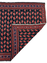 Persian Senneh Kilim rug with a dark blue field featuring repeating red geometric floral motifs and red and blue patterned borders, corner folded to show back side.