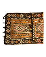 Folded vintage Persian Qashqai Kilim rug with geometric diamond patterns in earthy tones of brown, orange, pink, and cream, featuring tassels on one side.