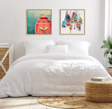 Minimalist bedroom with white bedding and two framed square paintings above the bed, one depicting a red canoe paddle and the other colorful fishing floats.