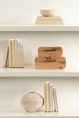 Two light wood stacking boxes with rounded edges and natural knots, placed on a white shelf alongside cream-colored books and a textured beige ceramic vase.